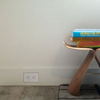 Concealed baseboard outlet next to modern stool with architecture books