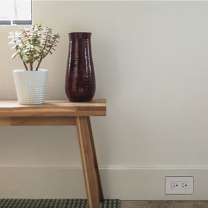 Hidden baseboard outlet in modern home adjacent bench, plant, vase & window